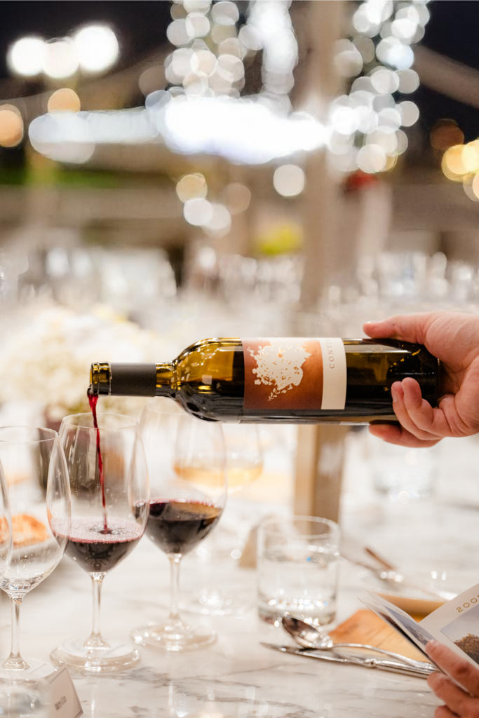 A bottle of Continuum wine being poured out into wine glasses